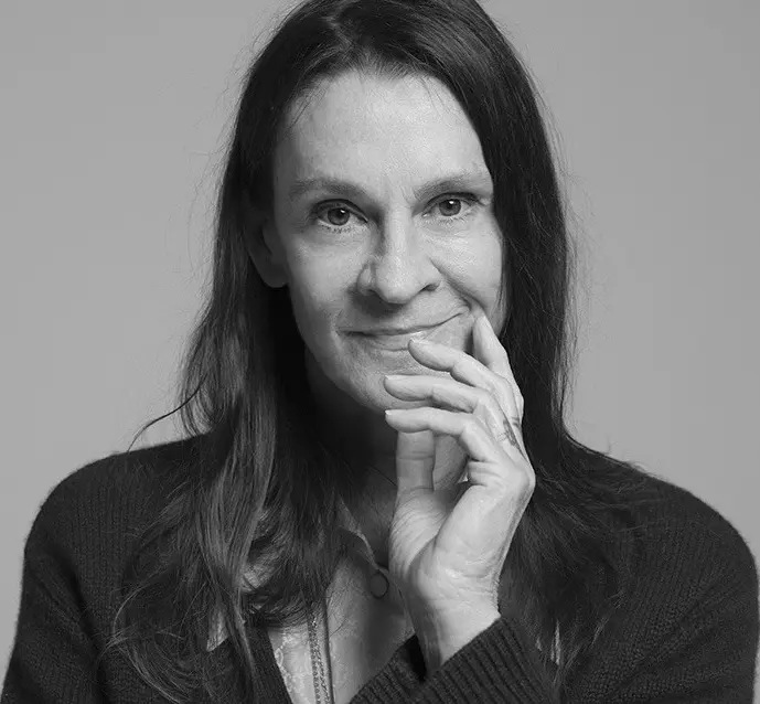 A woman with long hair is smiling and holding her hand to her face.